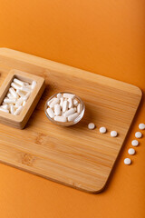 White vitamin pills in wooden bos and glass bowl from above on a wooden desk on orange bakcground.