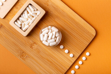 White vitamin pills in wooden bos and glass bowl from above on a wooden desk on orange bakcground.