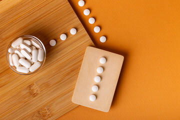 White vitamin pills in wooden bos and glass bowl from above on a wooden desk on orange bakcground.