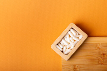 Nutritional supplements, vitamins and minerals. White vitamin pills in wooden box l from above on a wooden desk on orange background. Healthy lifestyle