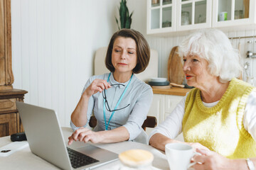 Indoor image of social worker and her senior female patient sitting at kitchen table, caregiver...