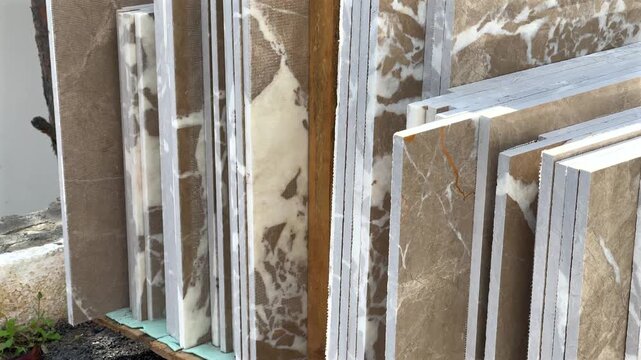 Various sizes and shades of beige and cream natural stone and marble slabs and tiles stacked vertically in a lumber rack at a construction supply or stone yard.