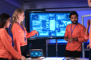 In a futuristic logistics control tower, a team manages the global supply chain, using a tablet and AI-powered dashboards to coordinate autonomous shipping and prevent disruptions.