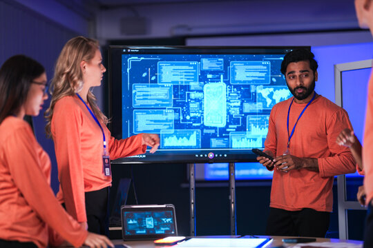 In a futuristic logistics control tower, a team manages the global supply chain, using a tablet and AI-powered dashboards to coordinate autonomous shipping and prevent disruptions. - Powered by Adobe