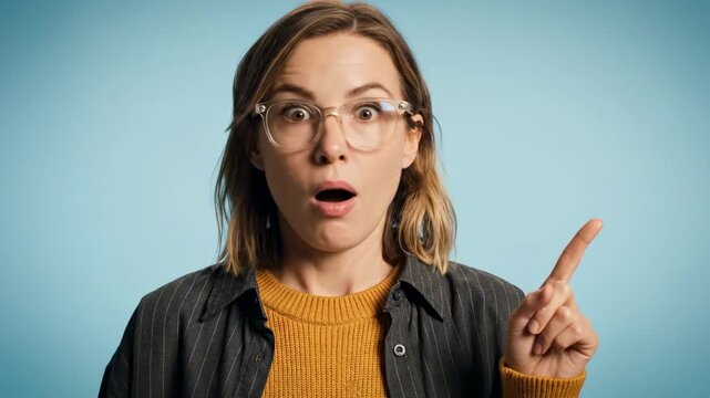 A surprised young woman with glasses and a shocked expression raises her finger in an excited gesture, set against a light blue background, conveying an unexpected realization or idea