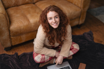 Young woman sits comfortably on the floor with laptop in cozy living room, enjoying a relaxed moment at home