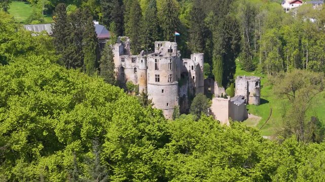 medieval castle beaufort les ch teaux de green cover old site town below cyclist runs road tall trees flag building pull drone shot back luxembourg 