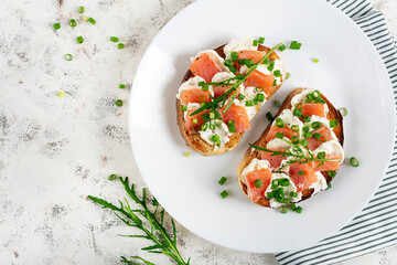 Two open sandwich, toast with salmon, cream cheese, green onions for healthy breakfast on white plate. Top view