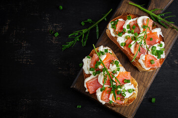 Salmon sandwiches, salted fish,  cream cheese and green onion on wooden background, top view. Healthy breakfast with salmon toasts