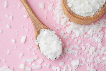 Wooden bowl and spoon with soy wax flakes on pastel pink background