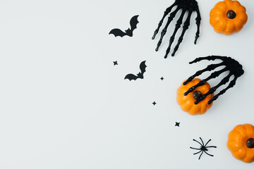 Black skeleton hands grab small orange pumpkins with bats and spiders on white background