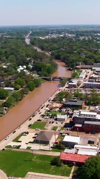 Vertical aerial shot looking down Bayou Teche toward Duperier Bridge, showing Fulton Street, business district, marina, and waterfront lodging in New Iberia, LA.