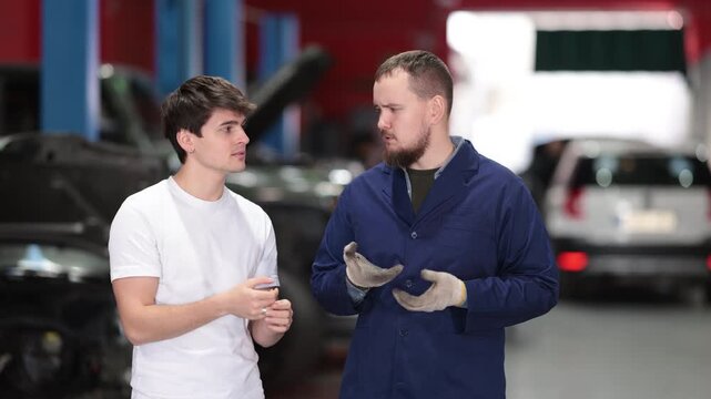  Young customer of a car service communicates about the process of repairing a car with a qualified mechanic. Specialist gives recommendations on oil changes, engine checks and tire changes