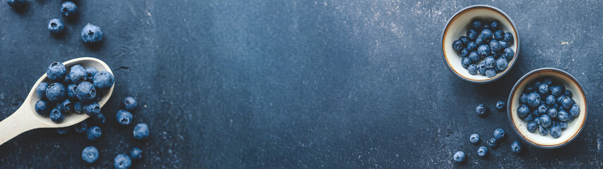 Fresh blueberries in wooden spoon and bowls on a dark textured background