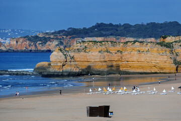 Sunny beach scene with rows of straw parasols and white lounge chairs on sand in Praia da Rocha in Portimao, Algarve, Portugal