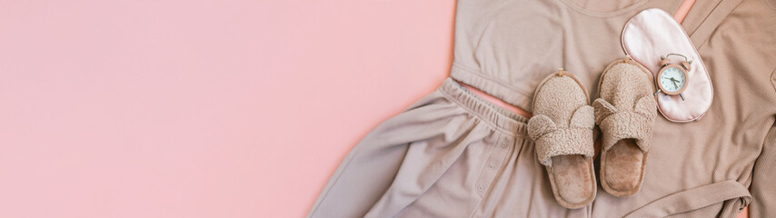 Cozy sleepwear set with slippers, eye mask, and alarm clock on a pink background