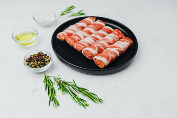 Bacon wrapped sausages on black plate with spices and rosemary
