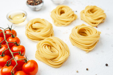 Raw tagliatelle pasta nests with tomatoes and spices on white background