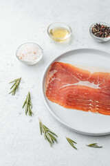 Prosciutto slices on white plate with rosemary and salt