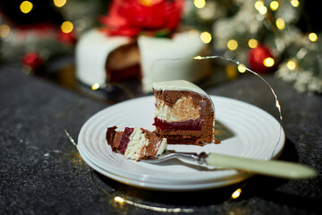A beautifully arranged plate holds a slice of decadent layered cake, showcasing red velvet and cream cheese layers, surrounded by twinkling lights and holiday decor.