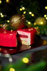 A slice of colorful layered dessert sits on a slate serving plate, surrounded by green pine branches and shimmering holiday decorations, evoking festive cheer.