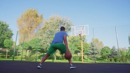 Low angle view of sporty fit African American male streetball player practicing basketball skills , dribbling ball , driving to the hoop for flying slam dunk and failing to score on outdoor court. - Powered by Adobe