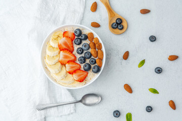 Oatmeal bowl with fruits and spoon and scattered nuts on table