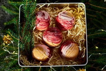 An elegant assortment of colorful dessert spheres is beautifully arranged in a festive gift box filled with straw and surrounded by fresh greenery and decorative touches, perfect for celebrations.