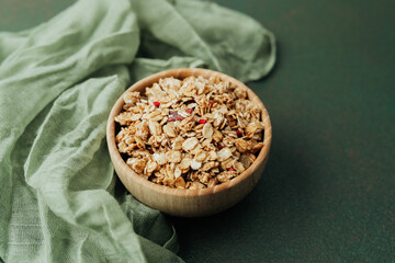 Granola in wooden bowl on green textile background