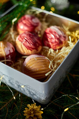 An elegant assortment of colorful dessert spheres is beautifully arranged in a festive gift box filled with straw and surrounded by fresh greenery and decorative touches, perfect for celebrations.