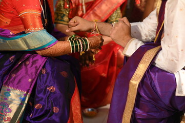 Hand of Indian bride Tie a Turmeric Thread Yellow knot on hand of groom. Close Up Hands of bride and Groom in hindu wedding. Marathi Wedding Ceremony. Maharashtra Culture. Hindu wedding rituals.