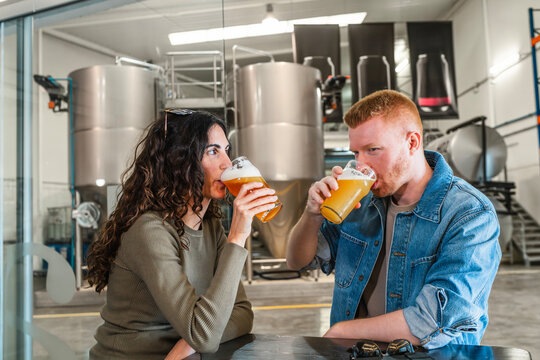 Young couple tasting craft beer inside a modern microbrewery, enjoying a relaxed tour and sampling fresh, artisanal brews