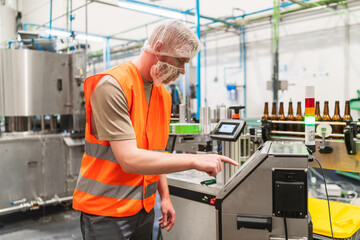Worker wearing protective gear operating a control panel on a bottling line, overseeing beer production in a brewery