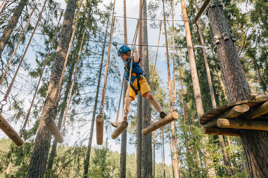 Boy balancing on hanging logs in forest high ropes course
