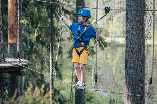 Smiling boy balancing on ropes in forest adventure park