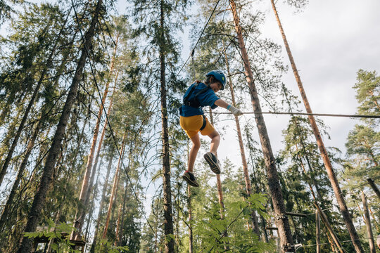 Boy jumping on safety line in forest high ropes course, smiling