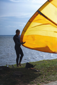 Kitesurfer in wetsuit holding large yellow kite on grassy shore