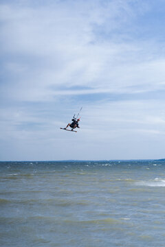 Kiteboarder performing aerial flip trick high above water, blue sky