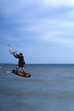 Man kitesurfer jumping high above the water with his board