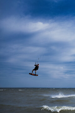 Kiteboarder performing aerial flip trick high above water, blue sky