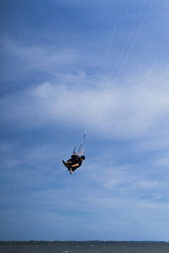 Kiteboarder performing aerial flip trick high above water, blue sky
