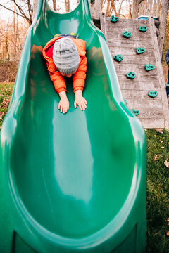 Young boy sliding headfirst on green playground slide