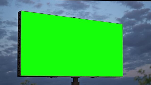 Blank billboard with green screen in evening light against cloudy sky, outdoor advertising mockup with chroma key copy space. 4K.