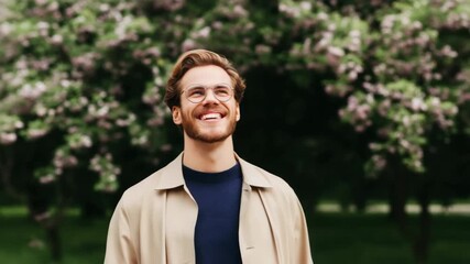 Smiling caucasian young male in glasses enjoying spring blossoms outdoors