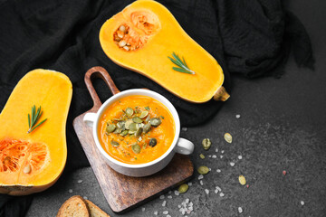 Butternut squash soup topped with seeds and rosemary next to halved squash on dark surface