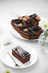 Rich chocolate cake slices with frosting on white plates next to white flowers