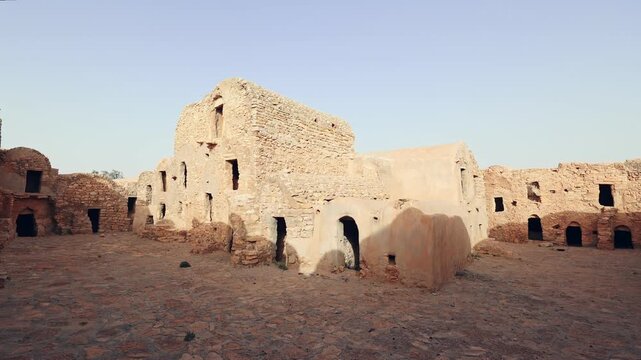 Remains of traditional ancient multi-level earthen mudbrick granaries with arched doorways in Ksar Daghar, bathed in sunshine under clear Tunisian sky