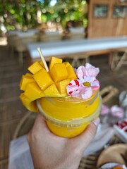 Hands of people holding mango smoothies and colorful flower bouquets