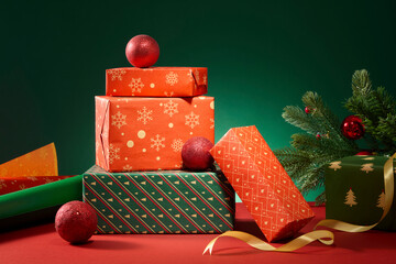 Christmas gift boxes stacked on a red background with green wrapping paper, pine branches and...
