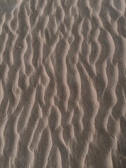 Wavy textured sand surface with natural light and shadows on beach ground. 